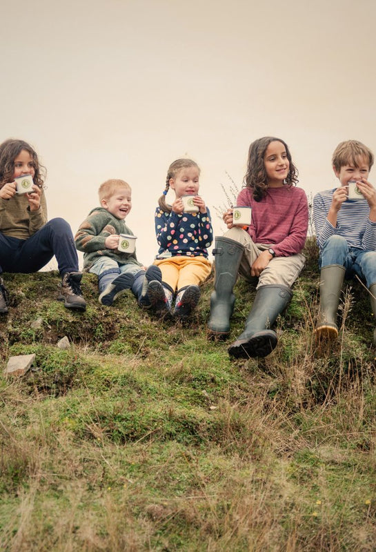 Children sitting on a grassy hill holding mugs.