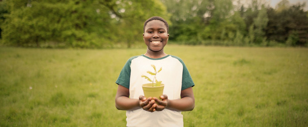 Person holding a potted plant in a grassy field