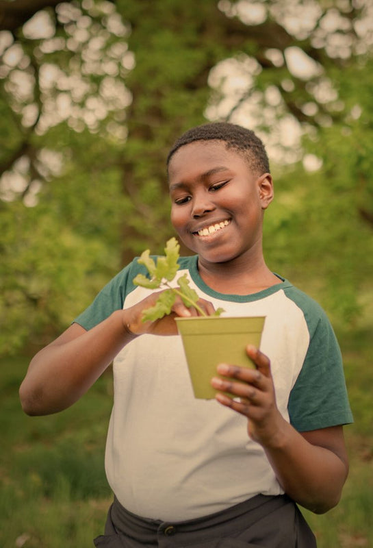 child holding a sapling in a green pot