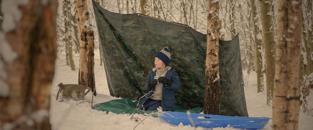 child in a camouflage den in the snow