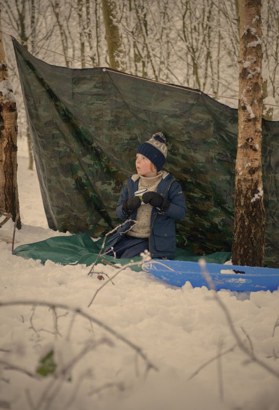 child in a camouflage den in the snow