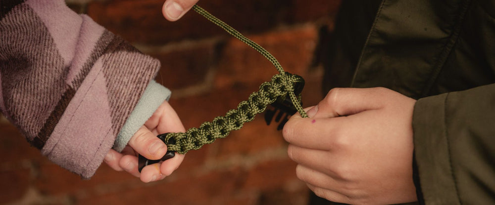 Two hands holding a green braided bracelet against a brick wall background