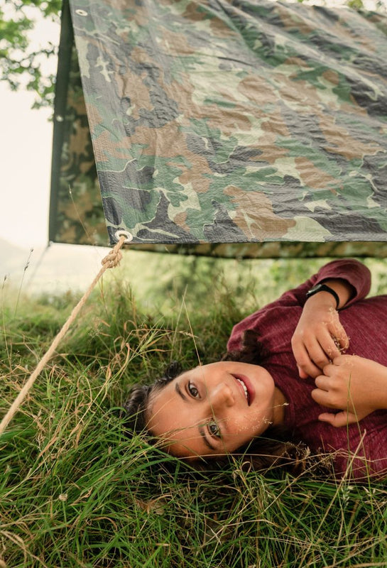 Child lying on grass under a camouflage tarp